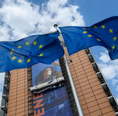 European Commission flags in front of the Berlaymont building with billboard